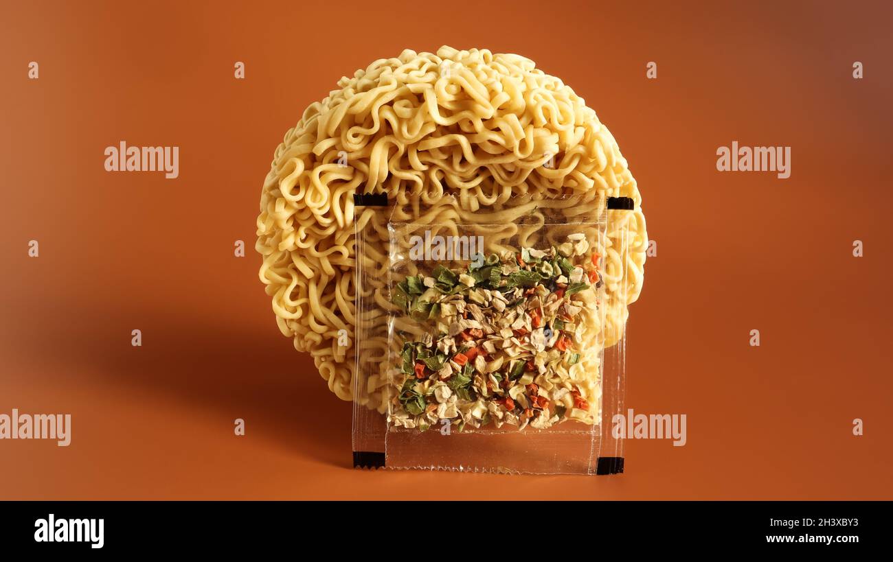 Cerchio di spaghetti istantanei con spezie crude su sfondo marrone chiaro. Cospargere vermicelli secchi cinesi o coreani con sale e s. Foto Stock