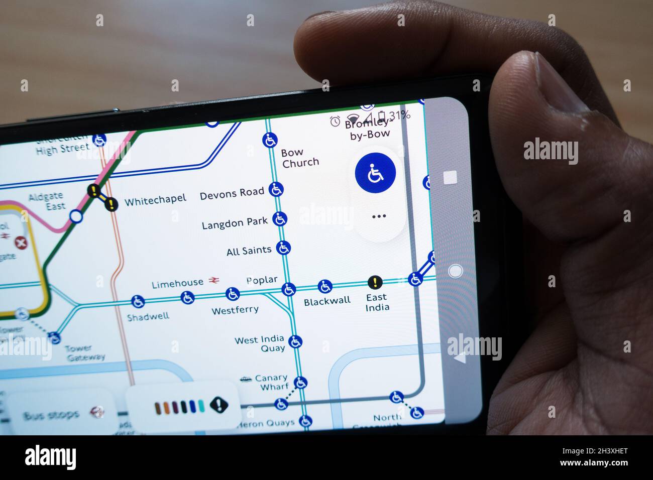 Uomo adulto che tiene uno smartphone con la mappa della metropolitana di Londra sul display controllando i collegamenti della stazione Foto Stock