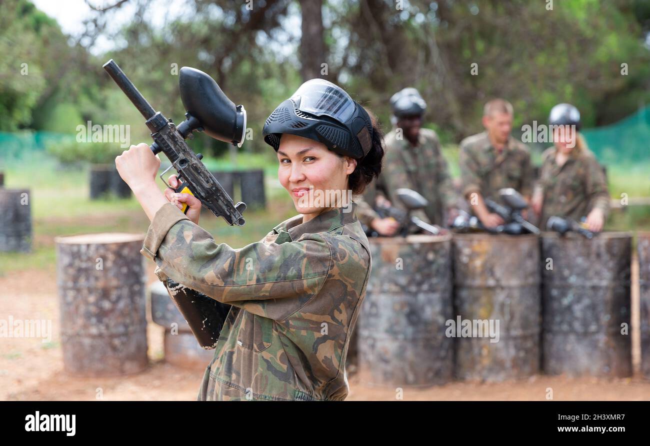 Donna sorridente con uniforme e pistola di tenuta pronta per giocare paintball con gli amici Foto Stock