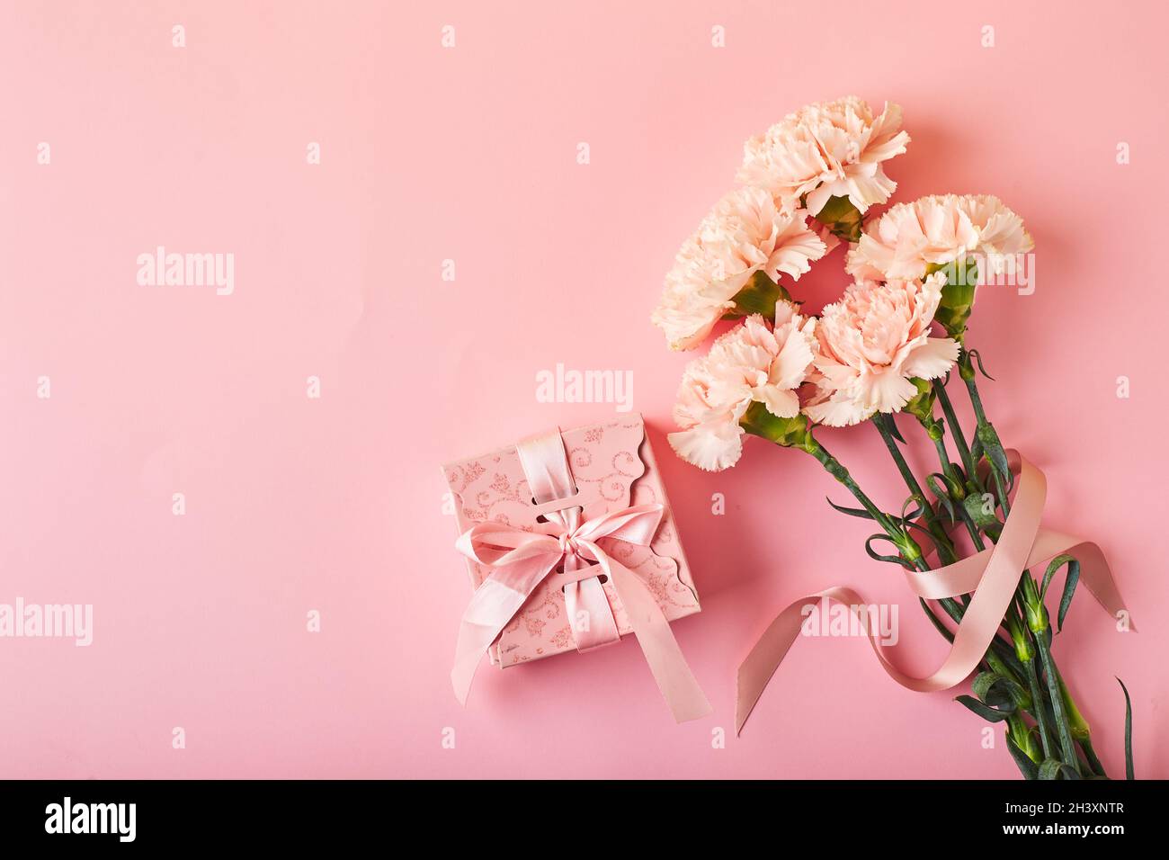 Bouquet di garofani rosa e scatola regalo rosa. Design concetto di saluto vacanza con bouquet garofano su sfondo rosa Foto Stock