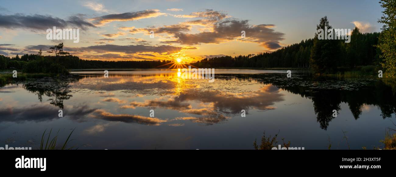 Un panorama di un tramonto colorato riflesso in un tranquillo paesaggio lacustre con foresta verde e canne Foto Stock