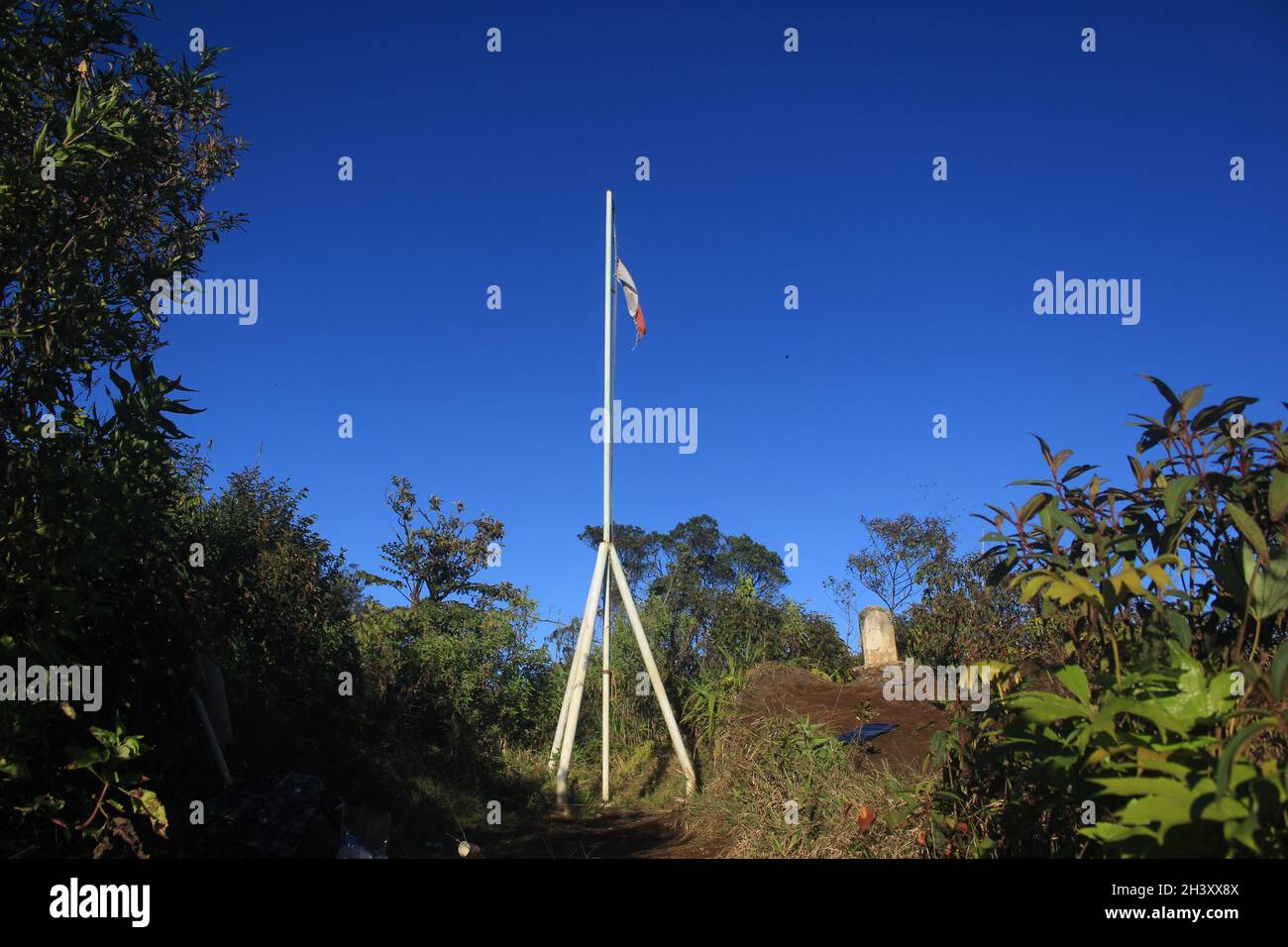 La bandiera rossa e bianca della Repubblica di Indonesia vola orgogliosamente sul monumento in ferro in cima al Monte Tugu, sullo sfondo blu cielo Foto Stock
