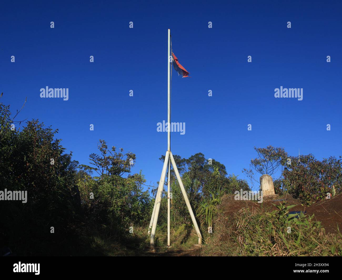 La bandiera rossa e bianca della Repubblica di Indonesia vola orgogliosamente sul monumento in ferro in cima al Monte Tugu, sullo sfondo blu cielo Foto Stock