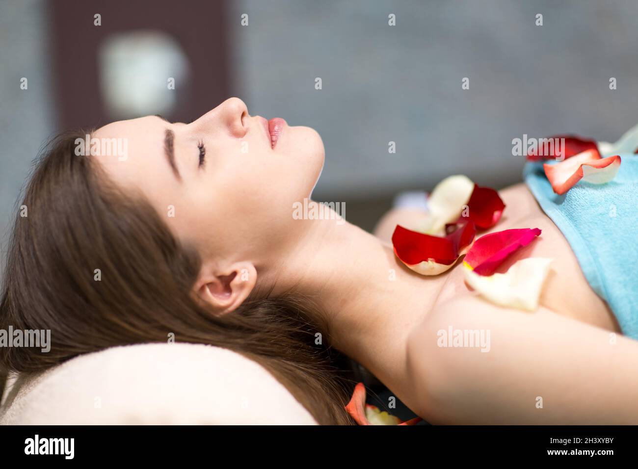 Giovane bella donna posa e relax in spa dopo massaggio con petali di rosa. Foto Stock