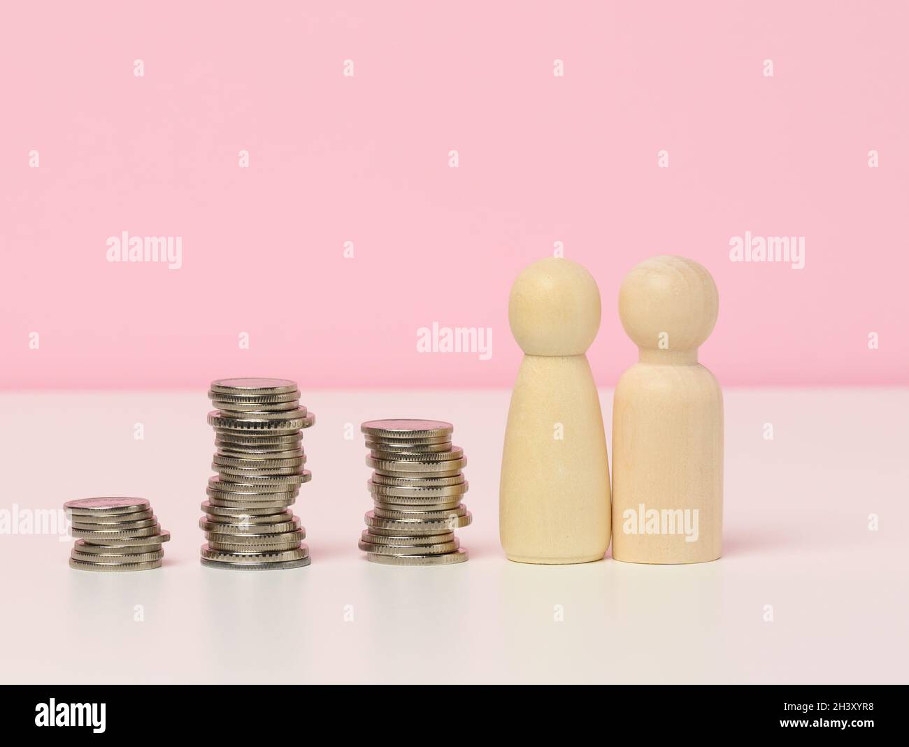 Una pila di monete metalliche e figure in legno di uomini su un tavolo bianco. Risparmi e spese, bilancio familiare, sussidi dello Stato Foto Stock