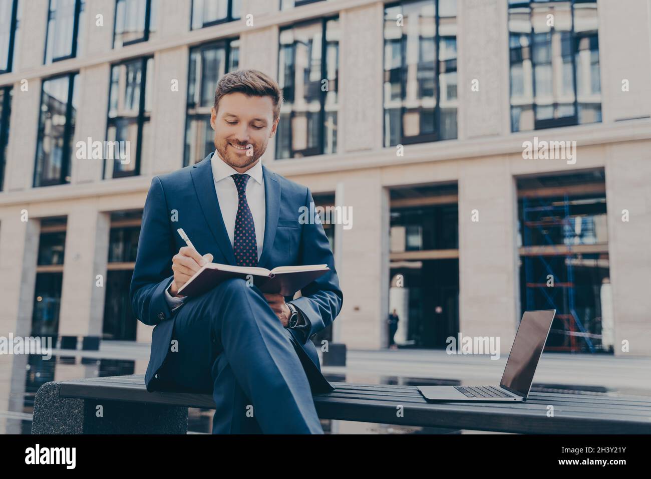 Il lavoratore professionale dell'ufficio che scrive le idee nel notebook mentre lavora in linea all'aperto Foto Stock