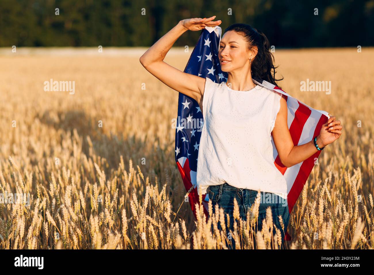 Donna con bandiera americana in campo di grano al tramonto. 4 luglio. Festa patriottica del giorno dell'indipendenza. Foto Stock