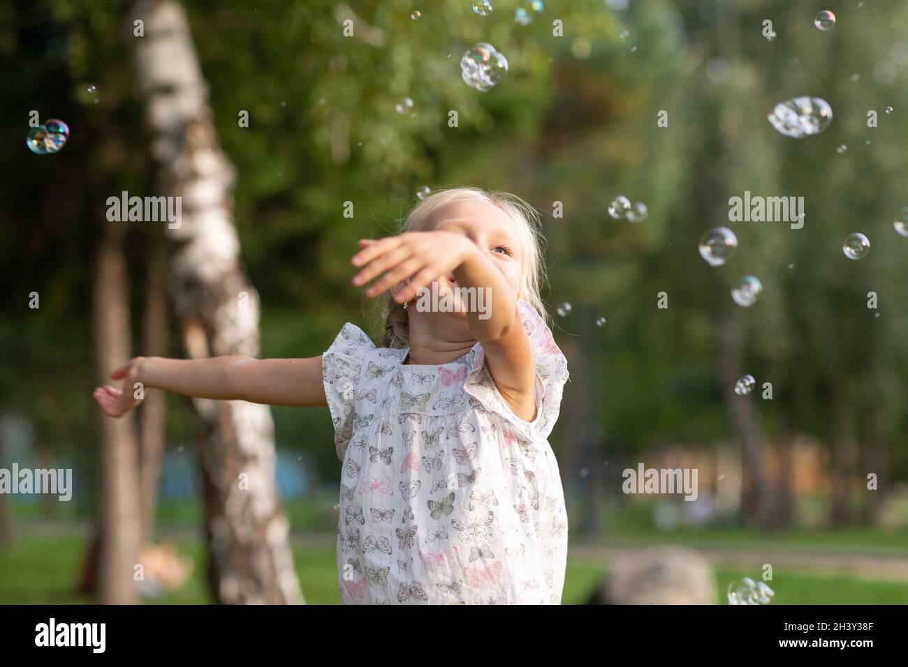 Ragazza carina piccola nel parco estivo che soffia bolle e. divertirsi Foto Stock
