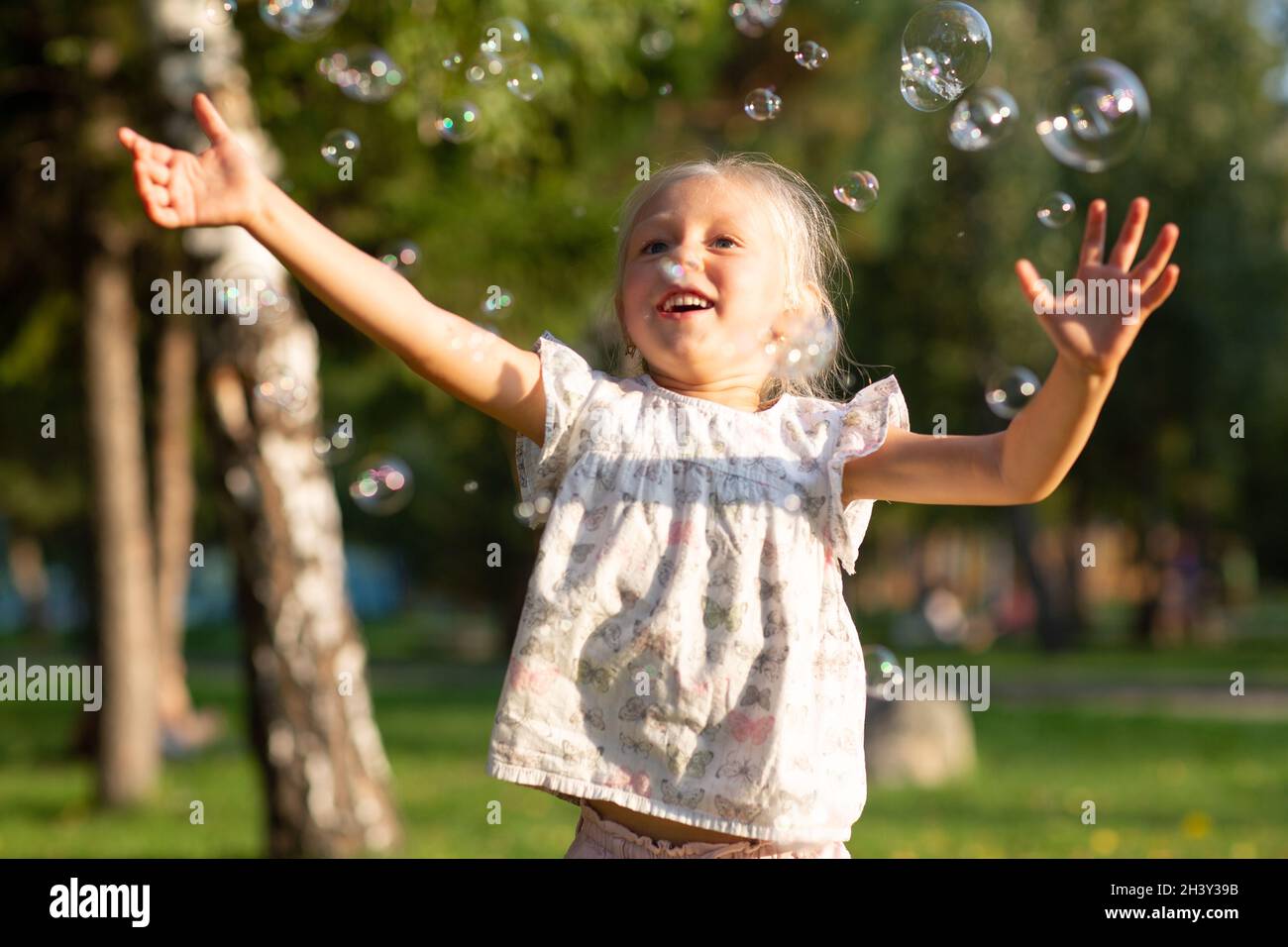 Ragazza carina piccola nel parco estivo che soffia bolle e. divertirsi Foto Stock