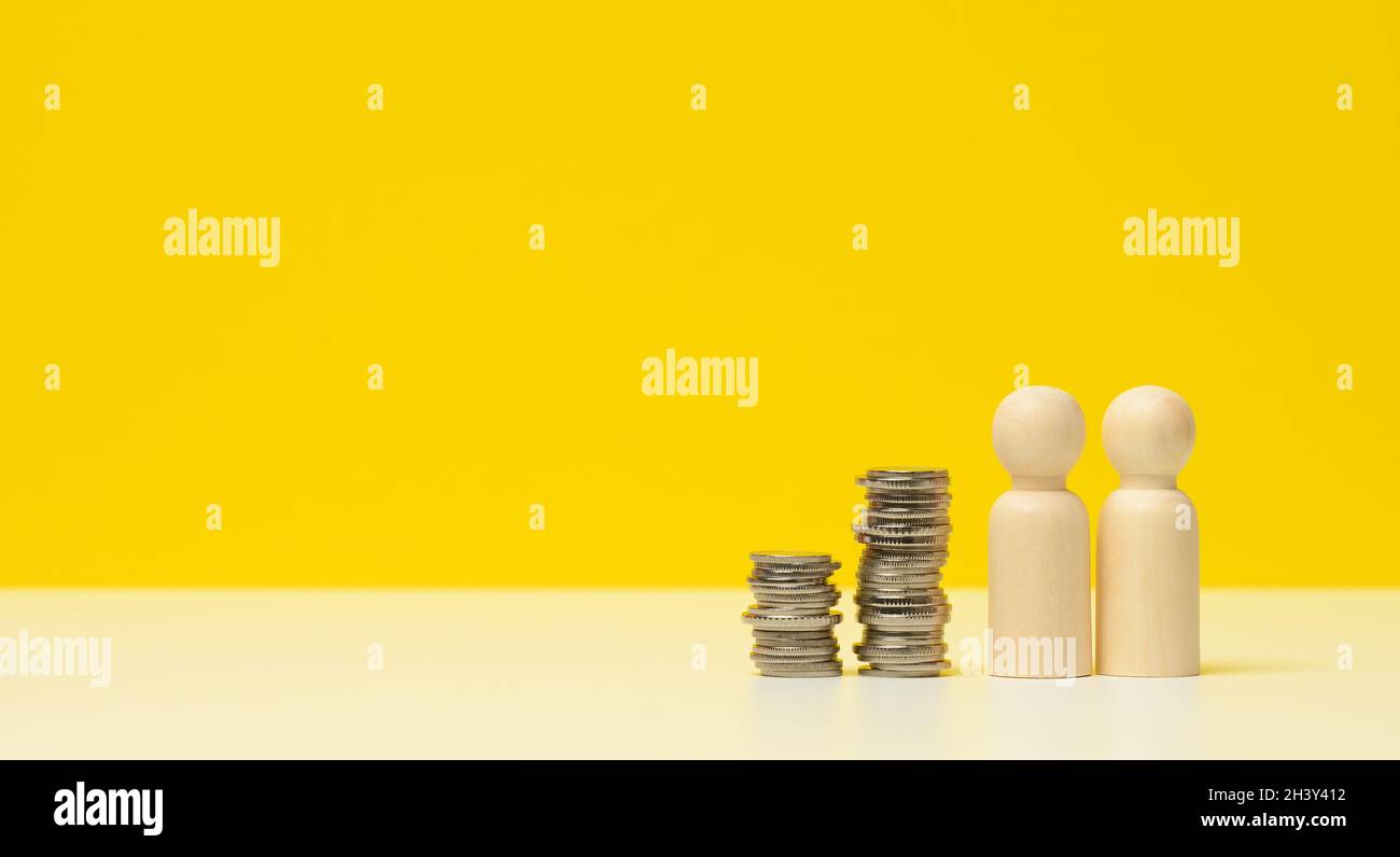 Pila di monete metalliche e figure in legno di uomini su un tavolo bianco. Risparmi e spese, bilancio familiare, sussidi dello Stato Foto Stock