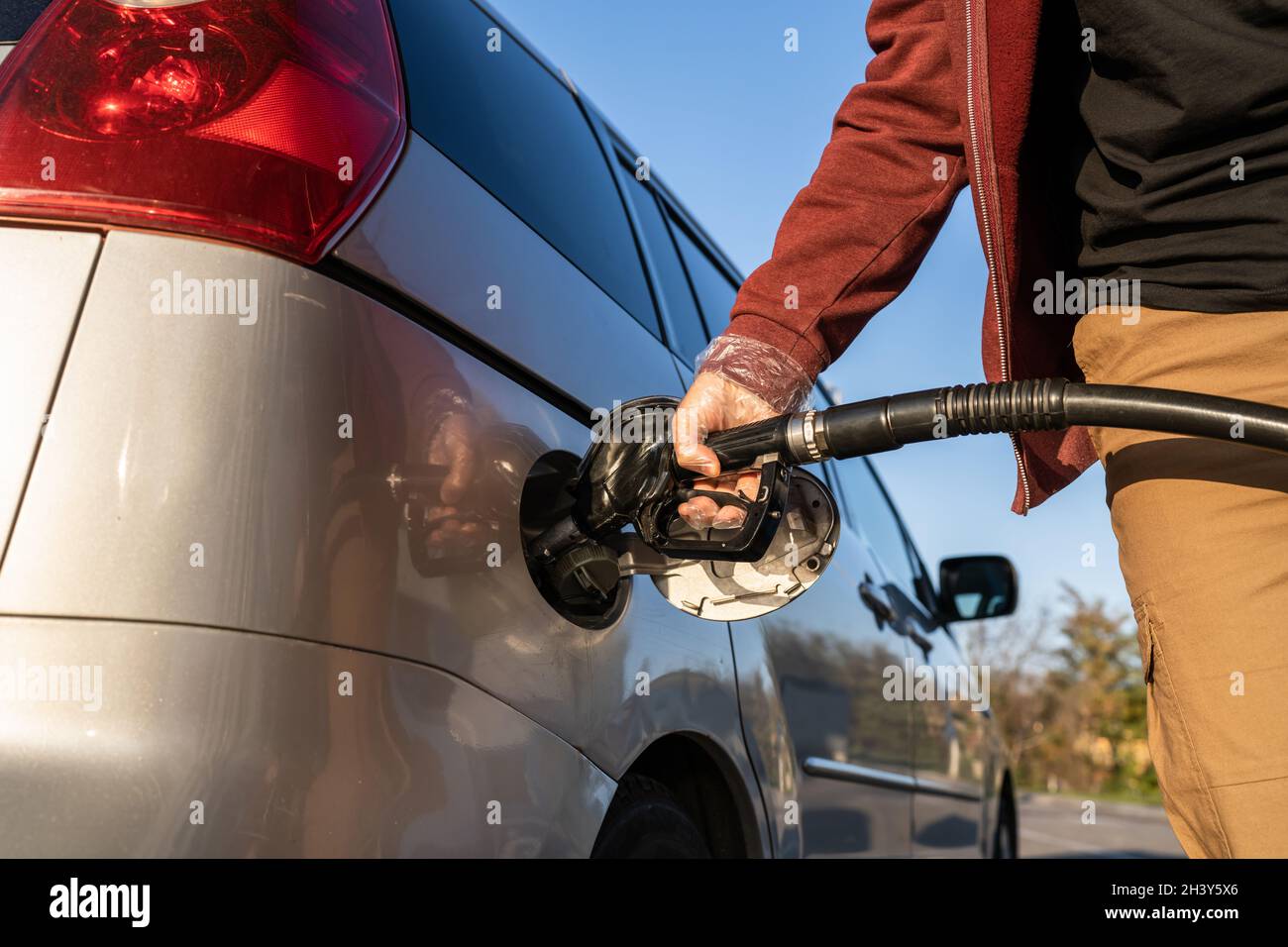 Primo piano a disposizione di un uomo caucasico sconosciuto tenere l'ugello nero della pompa del gas versando benzina nel serbatoio del carburante rifornimento di petrolio al veicolo in modalità self-service Foto Stock