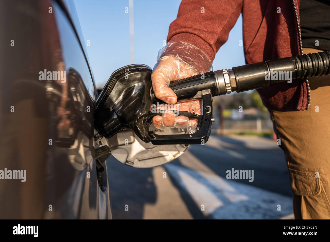 Primo piano a disposizione di un uomo caucasico sconosciuto tenere l'ugello nero della pompa del gas versando benzina nel serbatoio del carburante rifornimento di petrolio al veicolo in modalità self-service Foto Stock
