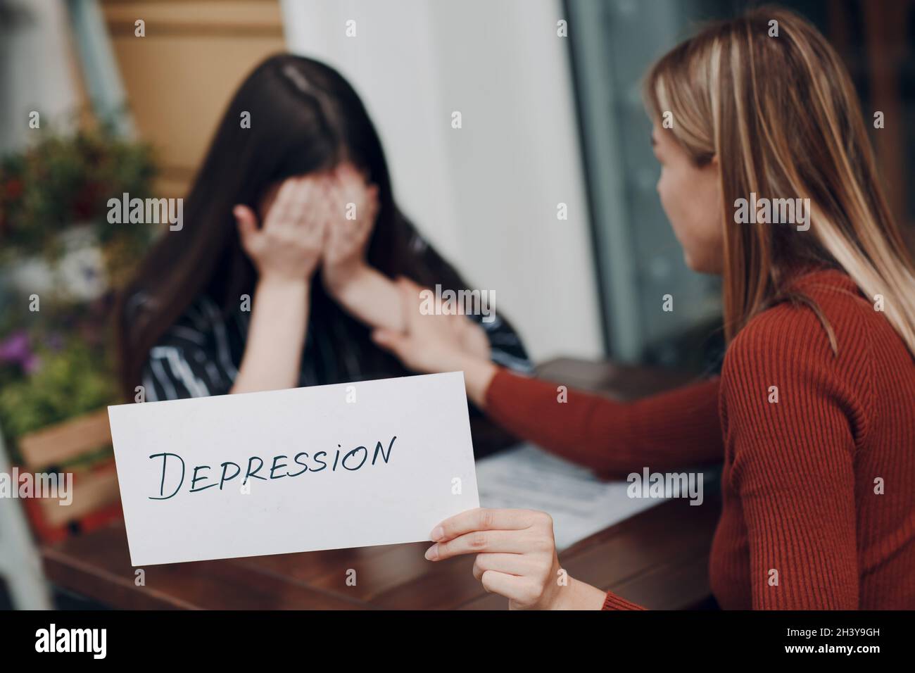 Concetto di depressione nascosta. Donna che piange. Seconda donna tenendo bianco foglio di carta etichettato parola depressione in mano. Due donne talki Foto Stock