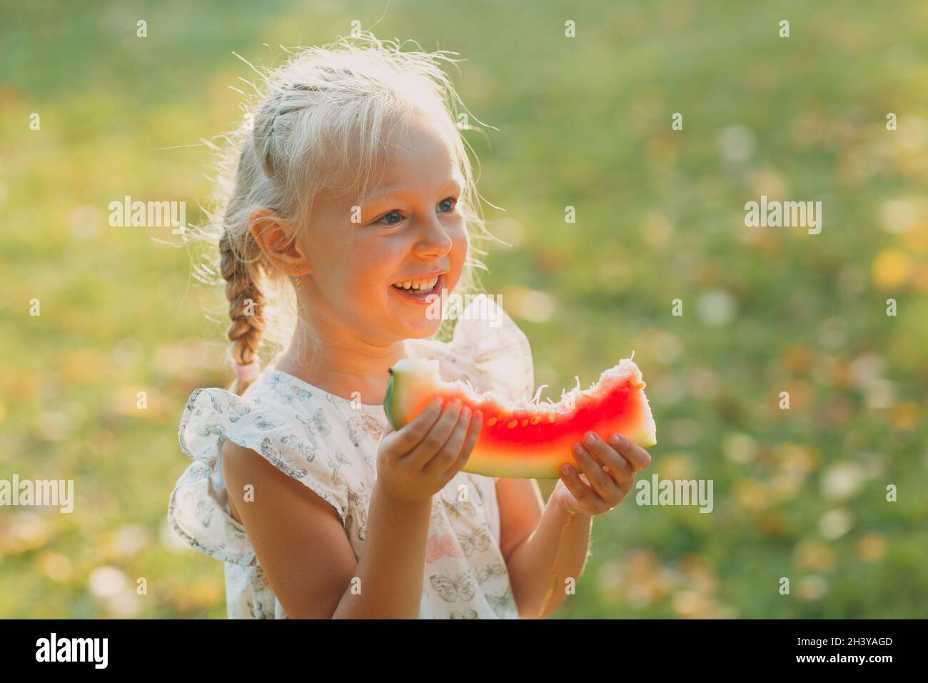 Carino bambina bionda con cocomero sull'erba dentro parcheggio Foto Stock