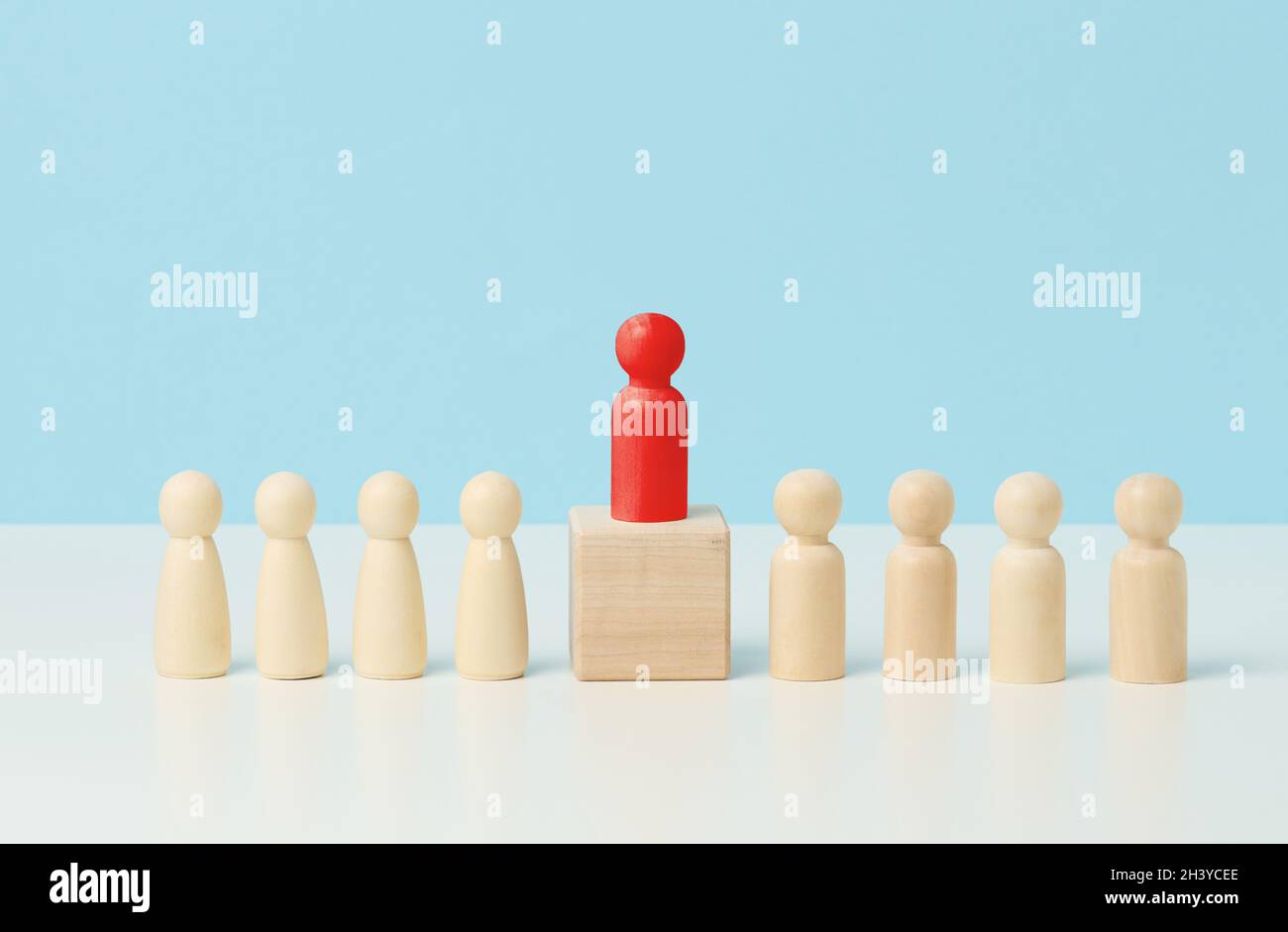 Piccoli uomini di legno su un tavolo bianco, rosso si erge su un cubo di legno. Ricerca di dipendenti di talento, rally, manipolazione della massa Foto Stock