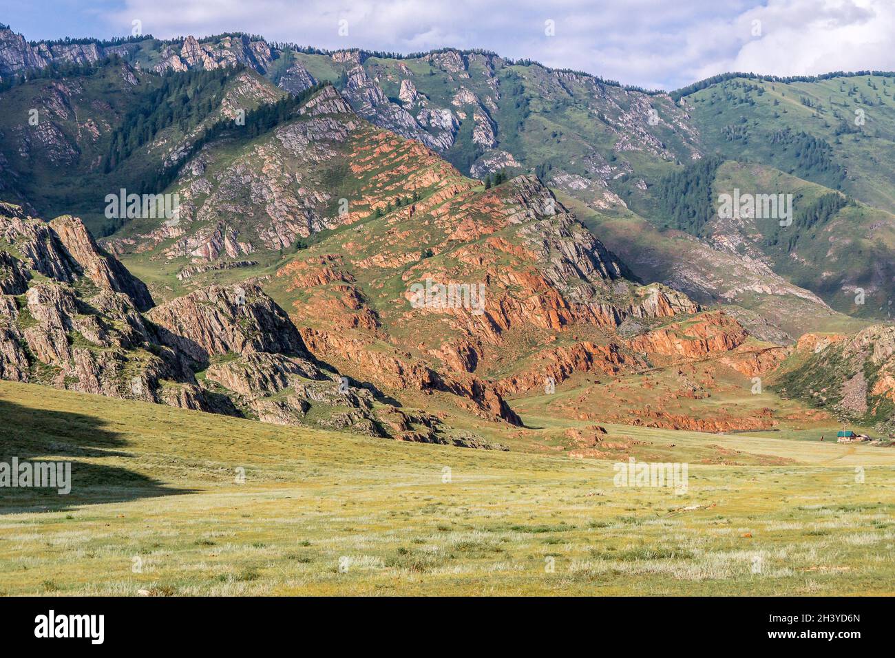 Affiorando uno strato inclinato di roccia rossa circondato da una roccia grigia. Una piccola casa di legno ai piedi della montagna. Foto Stock