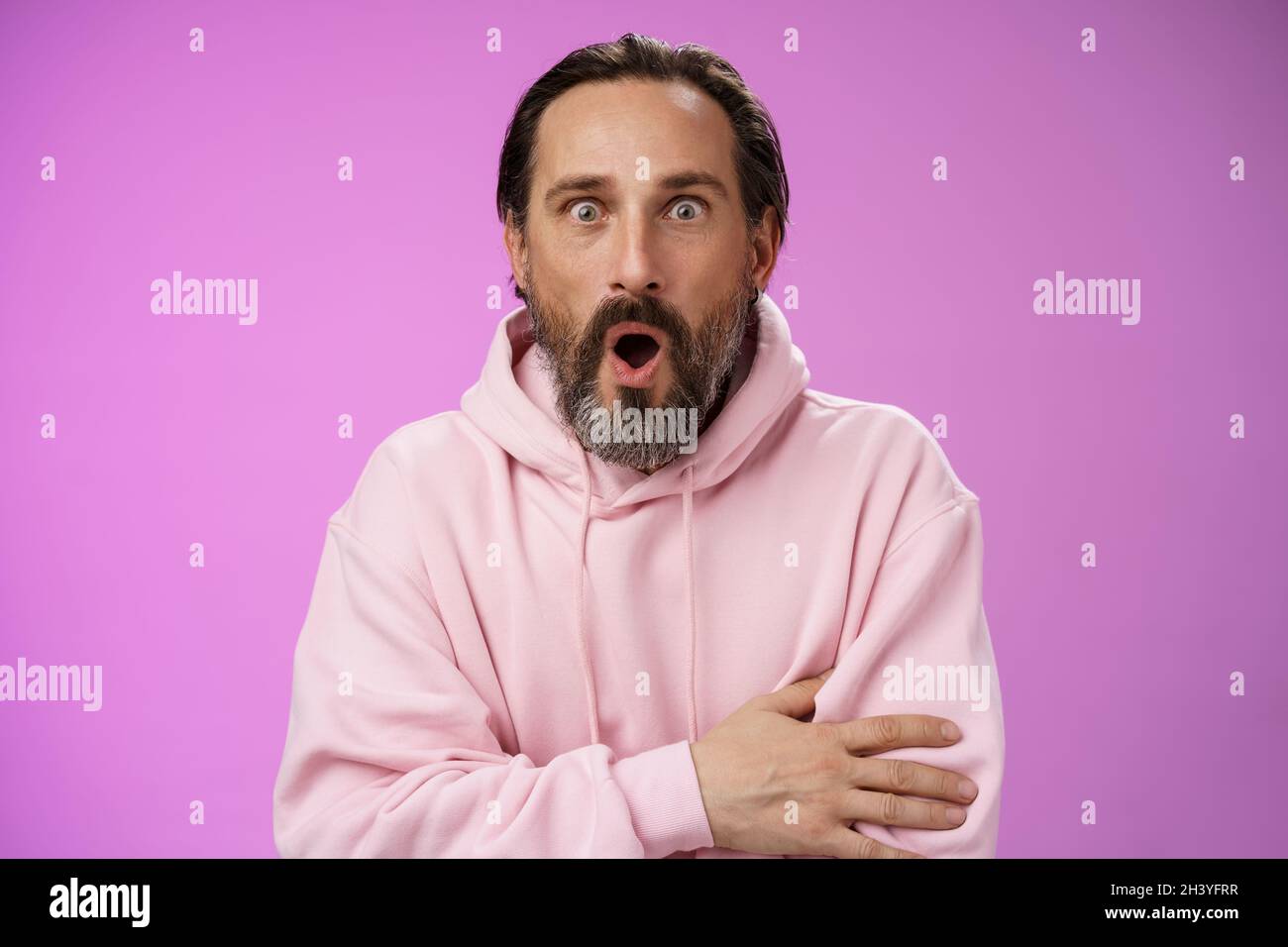 Shocked impressionato gossiping caucasico bearded adulto 40s capelli grigi dell'uomo in uncino rosa che gasping le labbra affascinate della piega wow allargano gli occhi Foto Stock