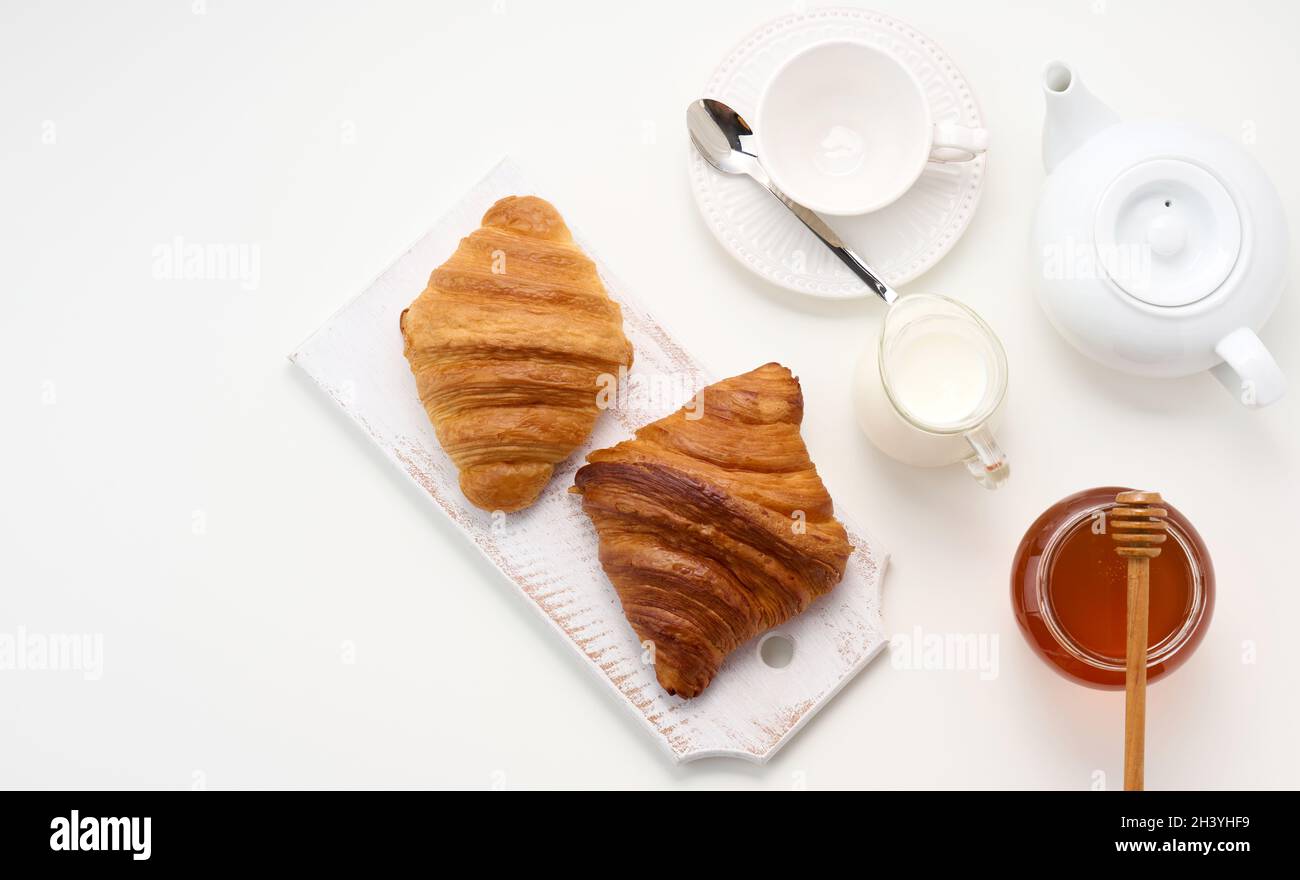 Croissant al forno, teiera in ceramica bianca e tazza e piattino vuoti,  vasetto di miele su un tavolo bianco, vista dall'alto Foto stock - Alamy