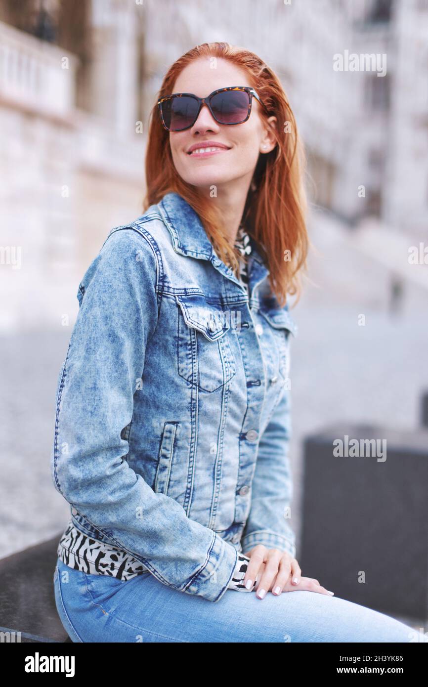 Giovane donna caucasica rossa in occhiali da sole che guarda via in città Foto Stock