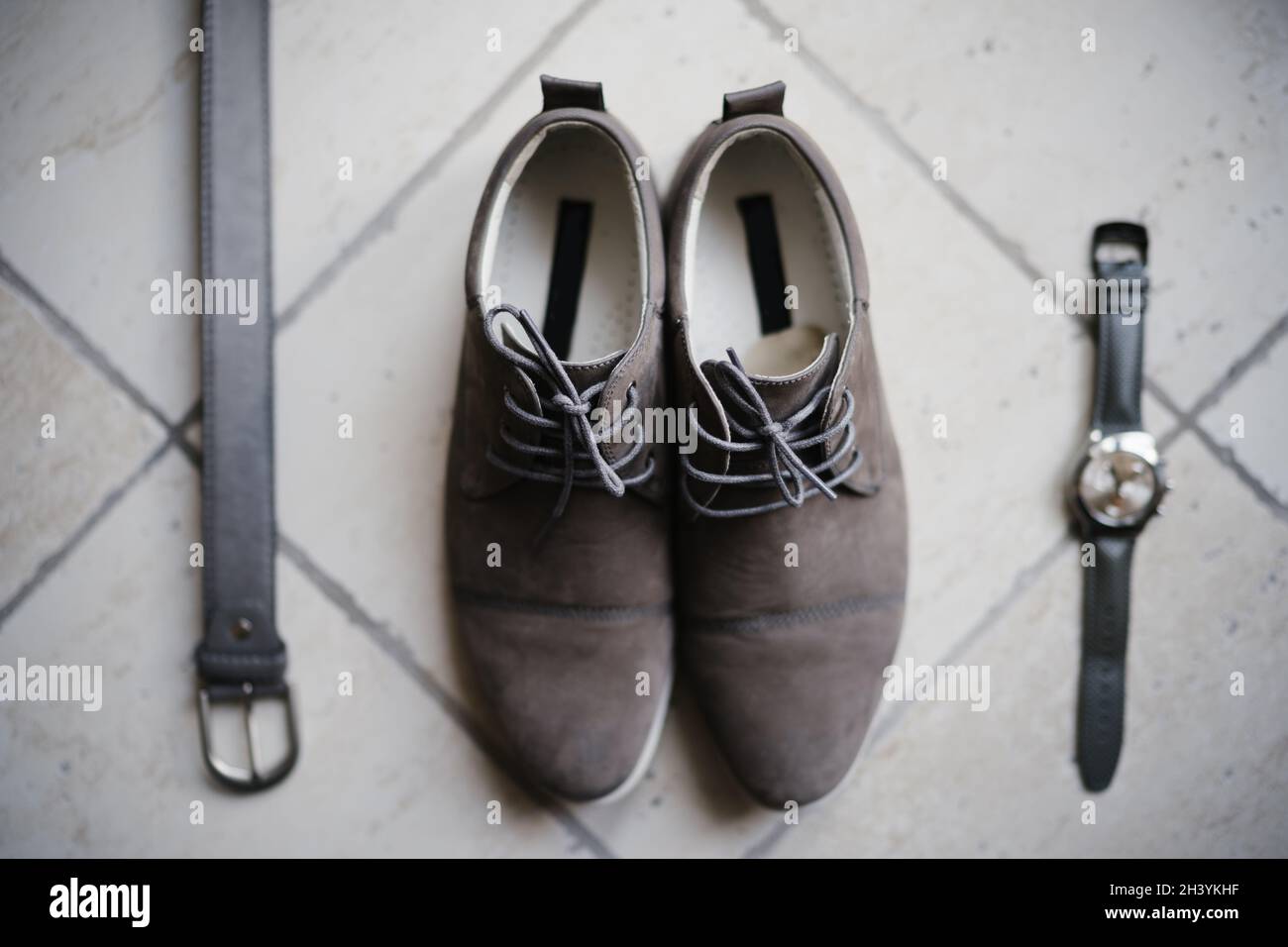 Scarpe, cintura e orologio da polso grigio derby camoscio da uomo su pavimento in pietra. Foto Stock