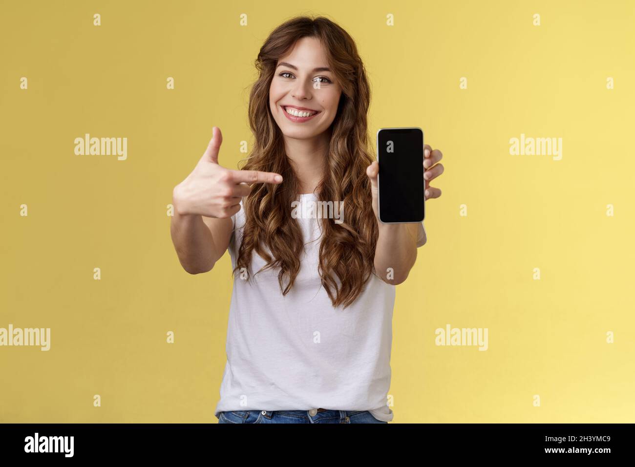 Ottimista sicuro buon aspetto femmina che mostra foto smartphone display tenere telefono cellulare esteso braccio fotocamera indice di puntamento finge Foto Stock