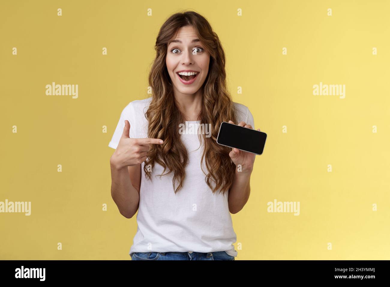 Allegro sorpreso cute fortunato ragazza battere miglior punteggio impressionante gioco mostrando smartphone display puntamento indice dito orizzontale scre Foto Stock