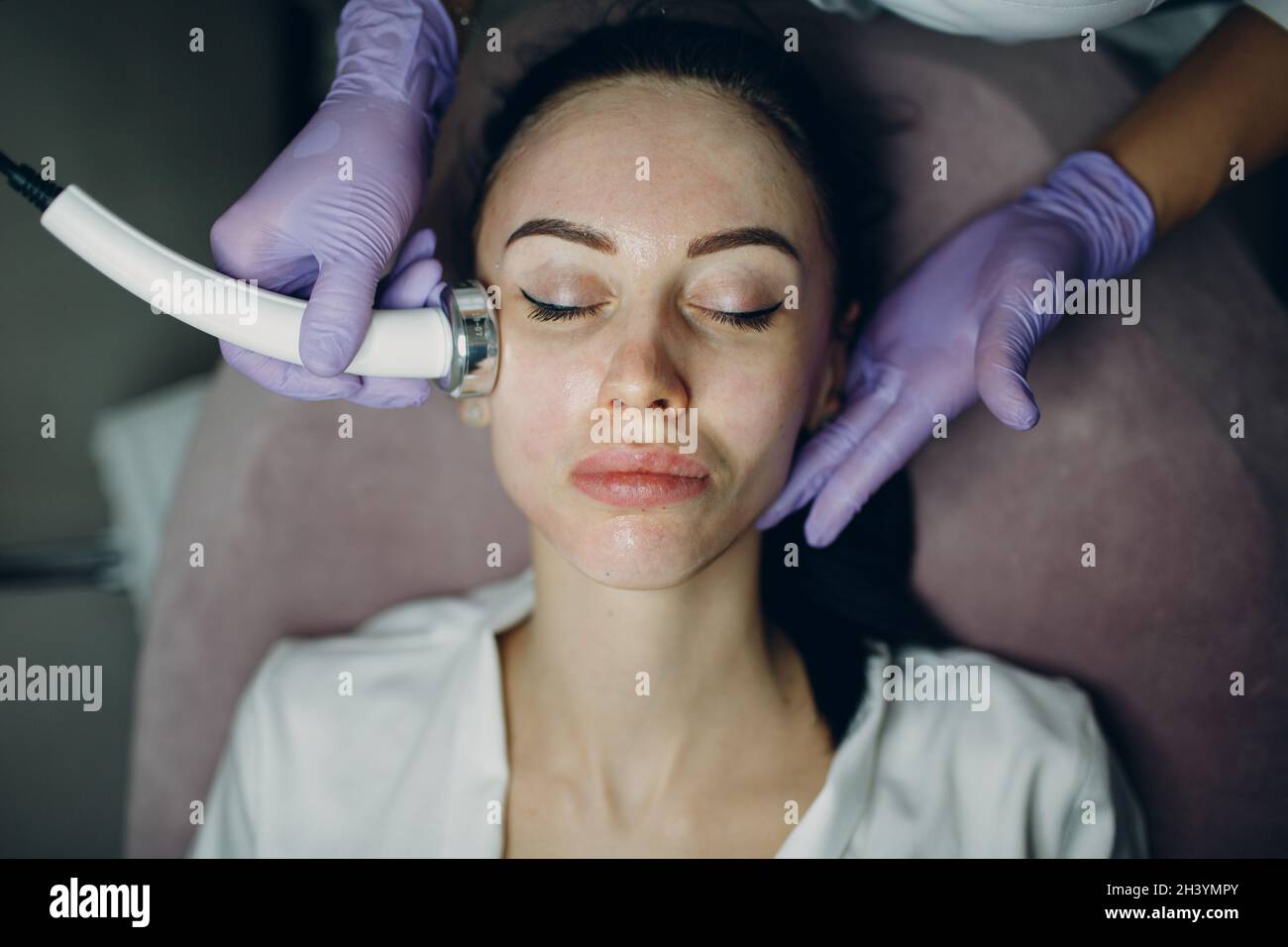 Primo piano della donna di testa che riceve la terapia facciale di phonoforesis di elettroporazione al salone di bellezza di centro termale. Foto Stock