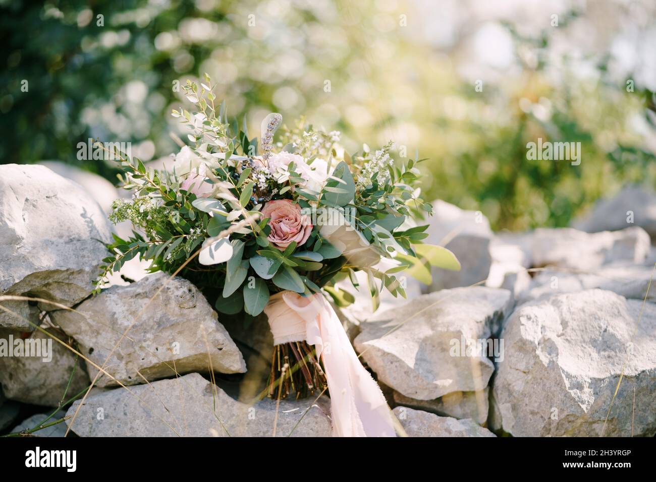 Bouquet nuziale di rose bianche e rosa, eustoma, rami di eucalipto e bosso, astilbe e nastri rosa sulle pietre Foto Stock