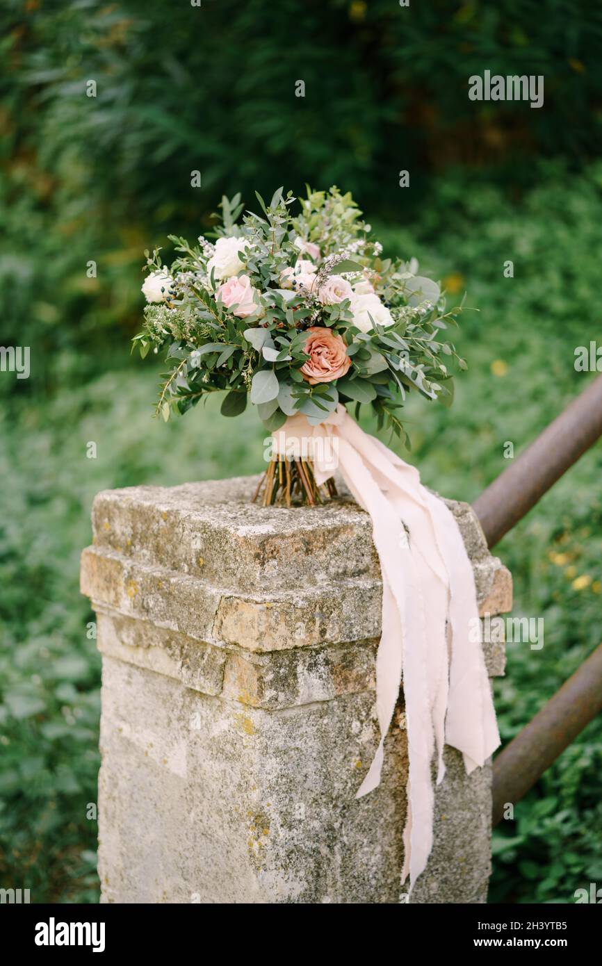 Bouquet nuziale di rose bianche e rosa, eustoma, rami di eucalipto e bosso, astilbe e nastri rosa su ringhiera di mattoni Foto Stock