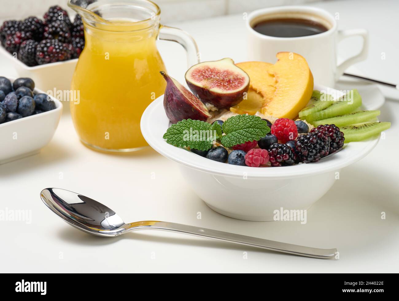 Piatto completo con farinata d'avena e frutta, succo appena spremuto in un decanter trasparente in vetro, tazza di caffè su un tavolo bianco. Healt Foto Stock