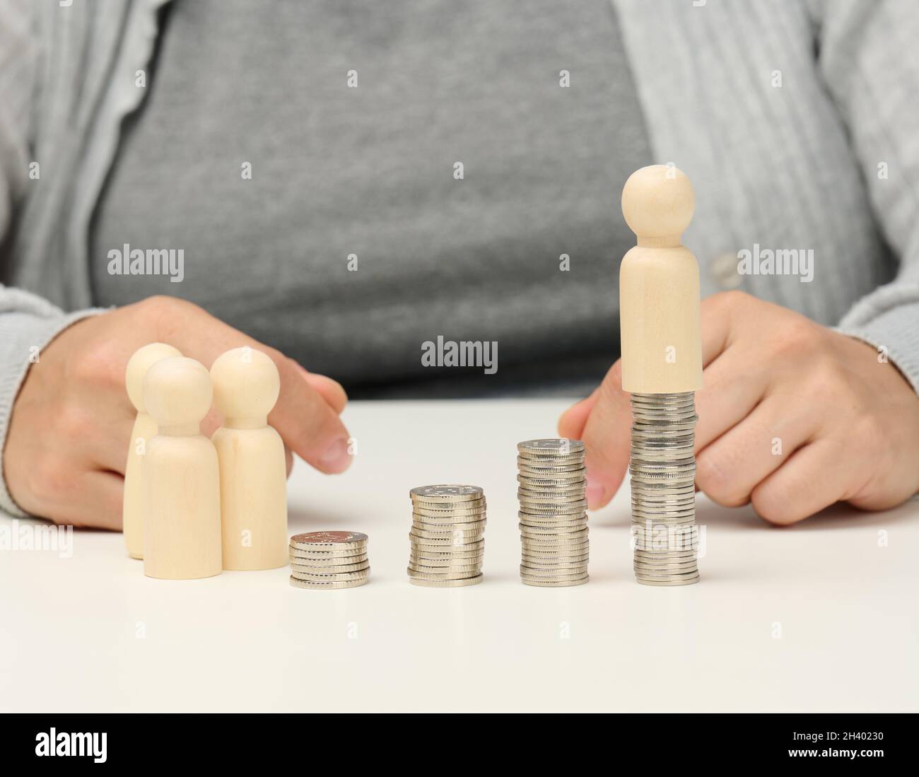 Pila di monete metalliche e figure in legno di uomini su un tavolo bianco. Risparmi e spese, bilancio familiare, sussidi dello Stato Foto Stock