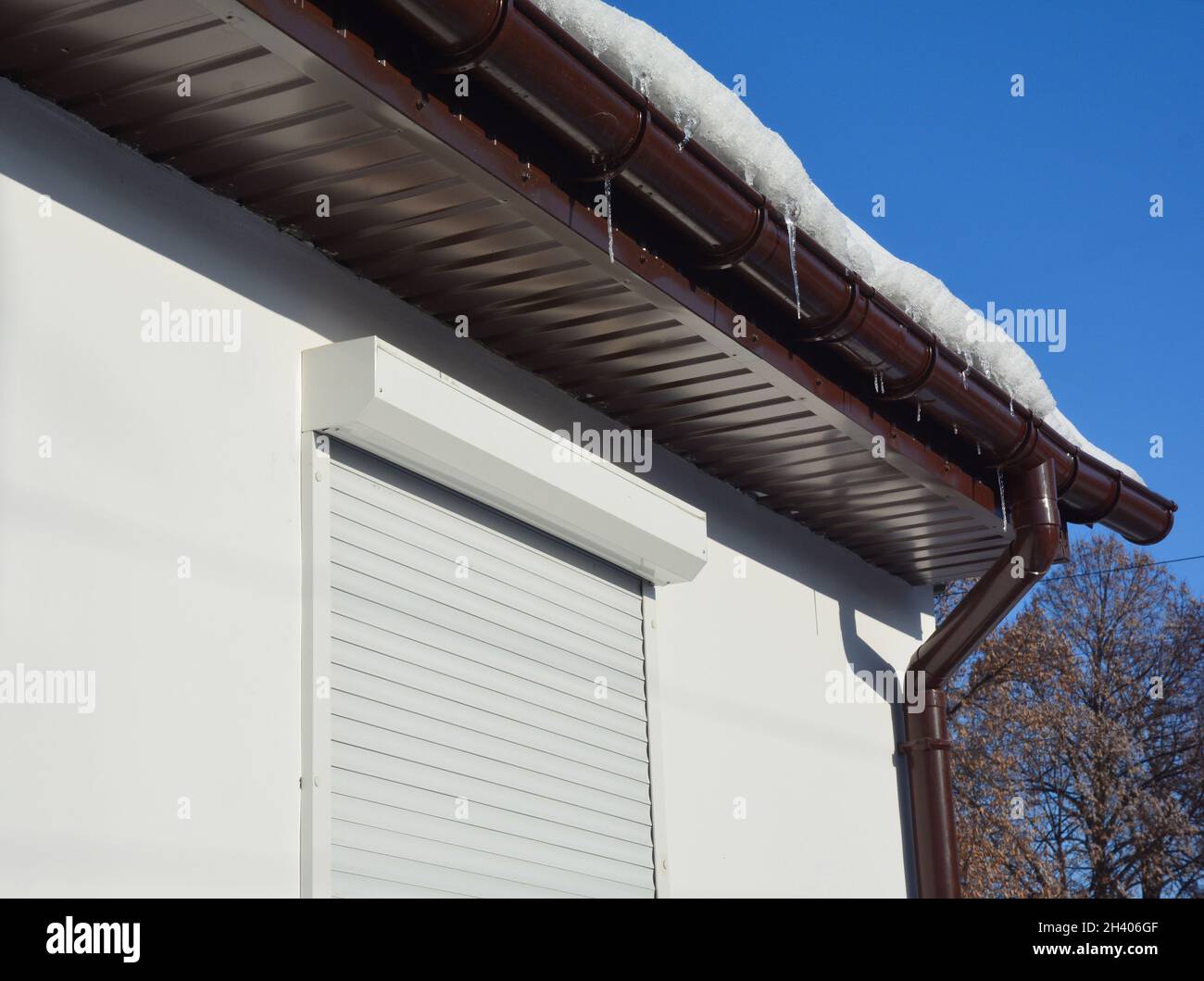 Gocciolatoio pieno di ghiaccio e neve in inverno. Ghiaccio congelato in una grondaia del tetto della casa, soffit di plastica e tapparelle per la protezione domestica. Foto Stock