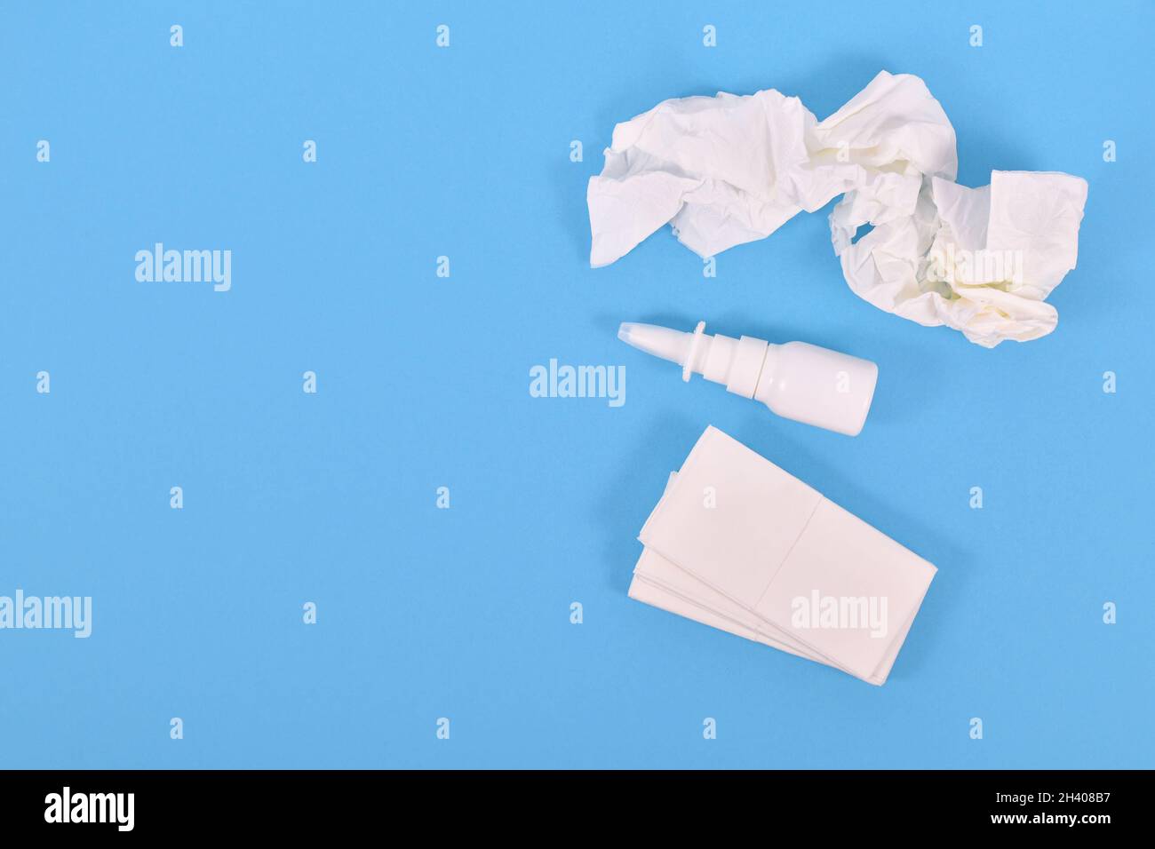 Vista dall'alto del flacone spray nasale e dei tessuti utilizzati durante il comune raffreddore su sfondo blu Foto Stock