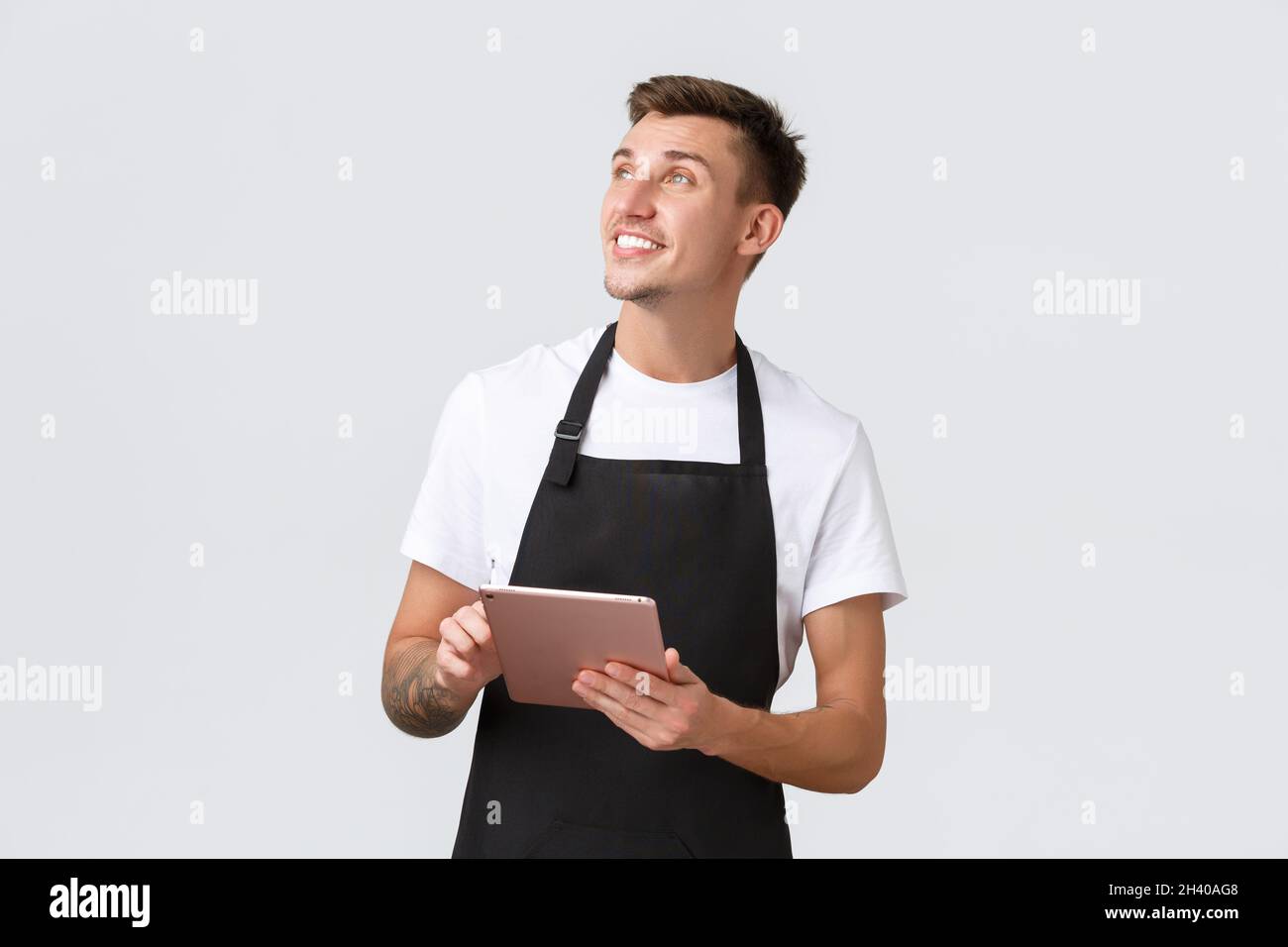 Concetto di piccola impresa, caffetteria e impiegati di cafe'. Simpatico ragazzo biondo, barista o cameriere in grembiule nero, lookin Foto Stock