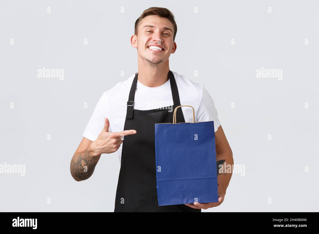 Concetto di negozio al dettaglio, shopping e dipendenti. Bel venditore allegro in negozio, il personale di panetteria punta il dito contro eco-borsa e SM Foto Stock