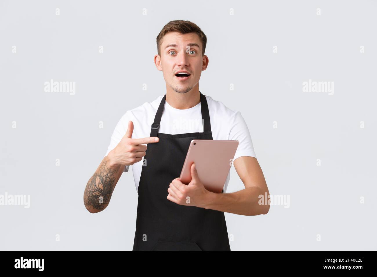 Concetto di piccola impresa, caffetteria e impiegati di cafe'. Bel cameriere o barista preoccupato in negozio che punta al tablet digitale, Foto Stock