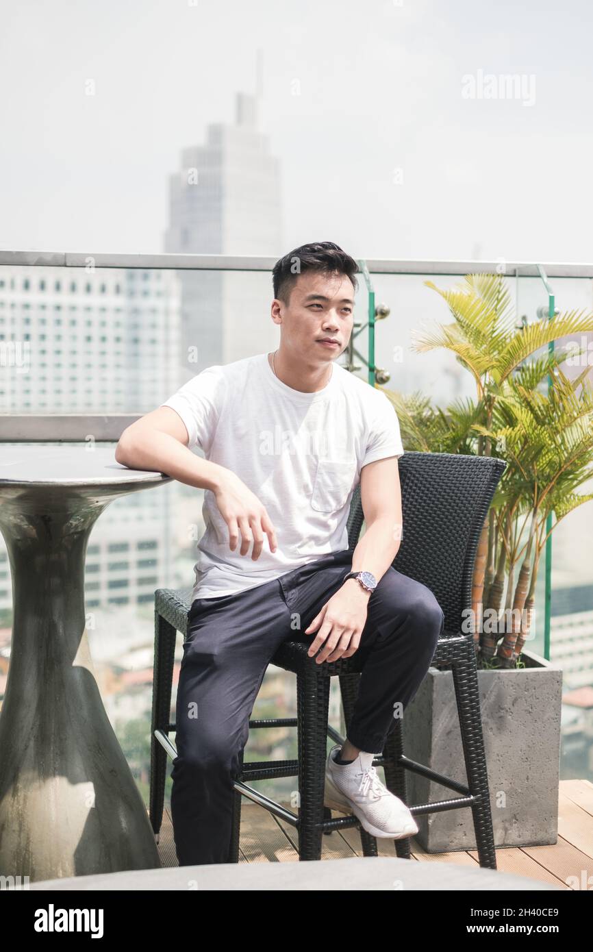 Bel giovane asiatico seduto sul tetto. Il ragazzo cinese, la vita millennial, lo stile di vita nella grande città, l'Asia moderna Foto Stock