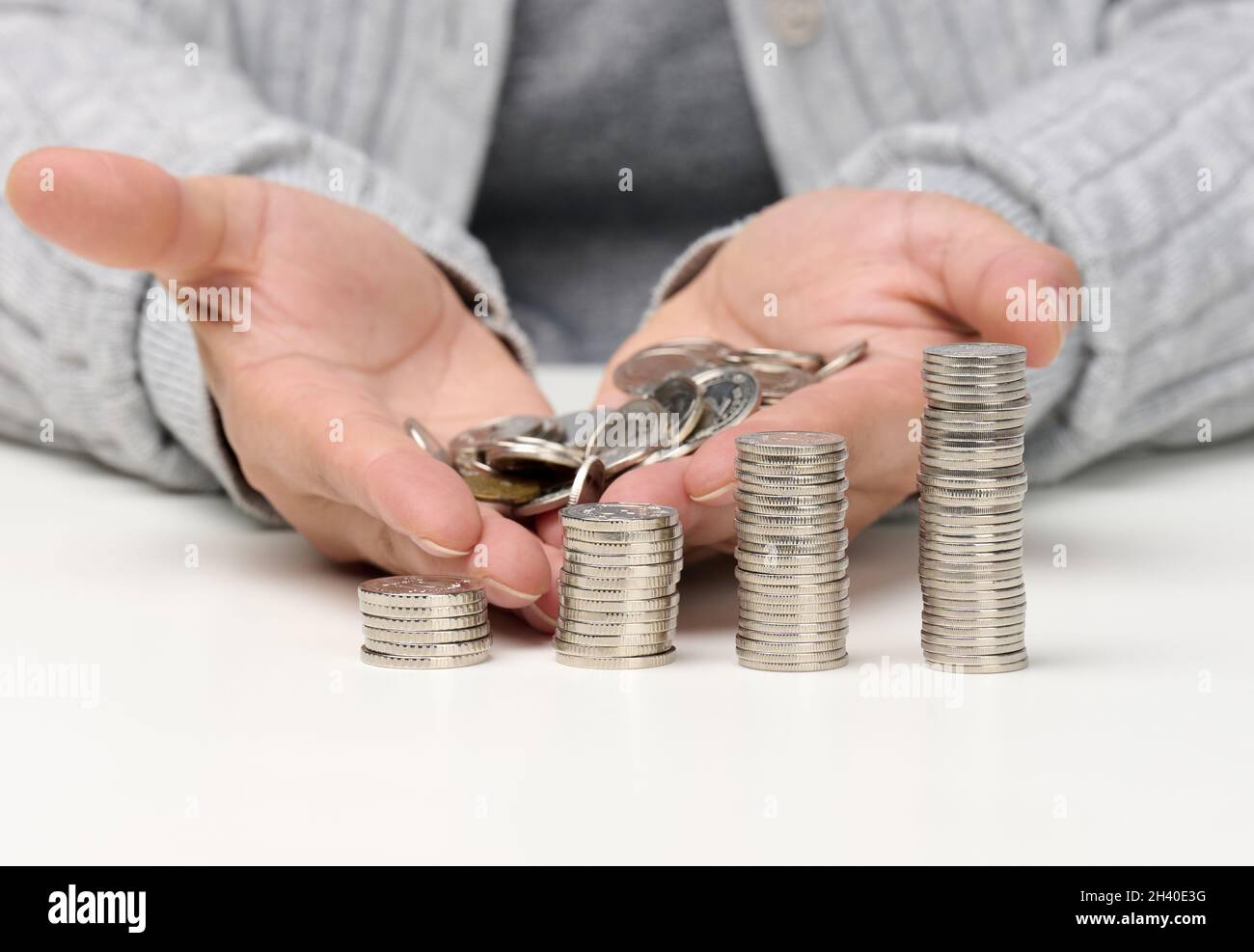 Pila di monete bianche e le mani femminili stanno tenendo un mucchio di monete. Povertà, pianificazione del bilancio. Sovvenzioni e basso salario Foto Stock