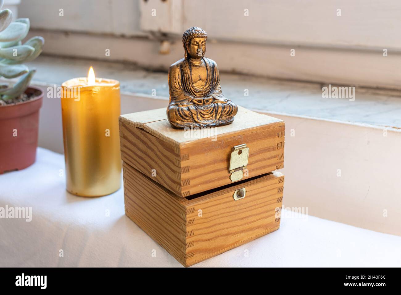 Statua di Buddha Zen seduta meditating su sfondo bianco. Pietre a lume di candela e petto sullo sfondo Foto Stock