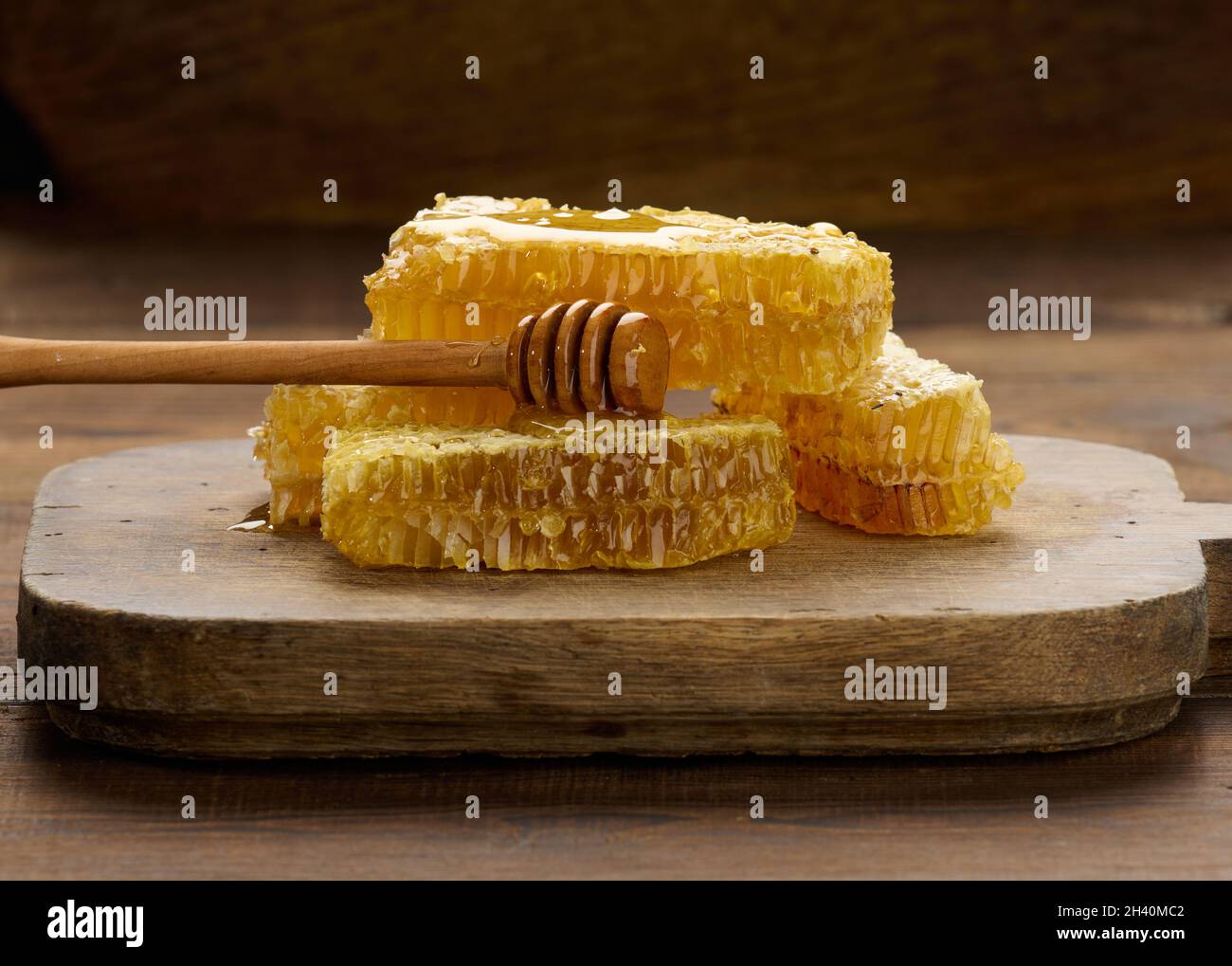 Cera a nido d'ape con miele su un asse nero e un cucchiaio di legno, tavola marrone Foto Stock