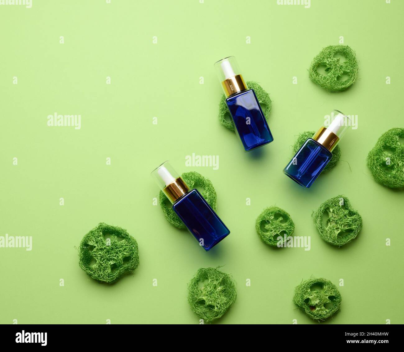 Bottiglia in vetro blu con contagocce per cosmetici su sfondo verde. Imballaggio per gel, siero, pubblicità e promozione. Foto Stock