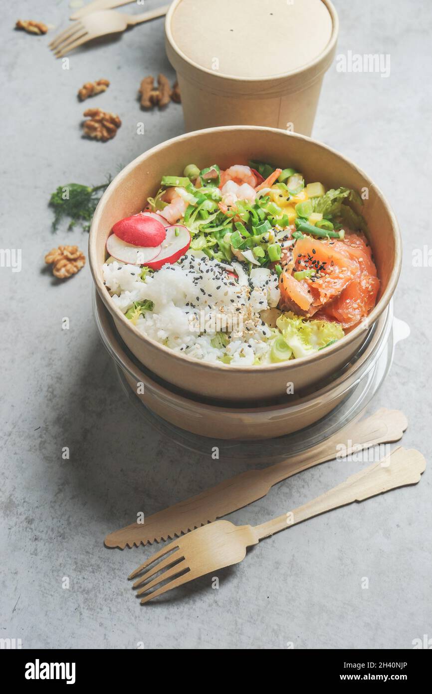 Insalata sana con salmone in confezione ecologica su tavolo da cucina grigio con posate in legno. Da asporto per il pranzo senza sprechi di imballaggio. Vista superiore Foto Stock