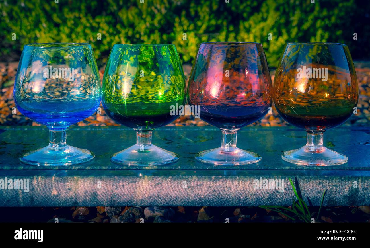 Una selezione di colorati bicchieri di brandy o liquore in fila su una lastra di granito in un giardino lussureggiante Foto Stock