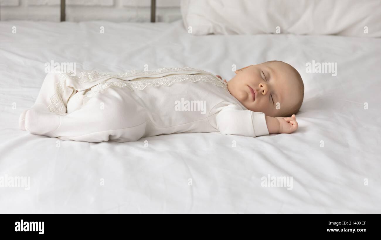 Bambino carino in bodysuit bianco che dorme sul letto comodo Foto Stock