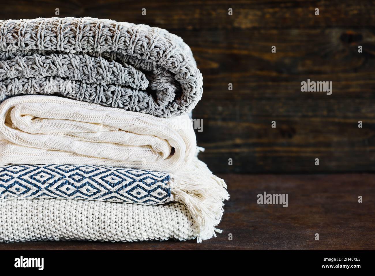 Accatastate coperte a maglia morbida contro uno sfondo rustico con messa a fuoco selettiva e sfondo sfocato. Spazio per fotocopie. Foto Stock