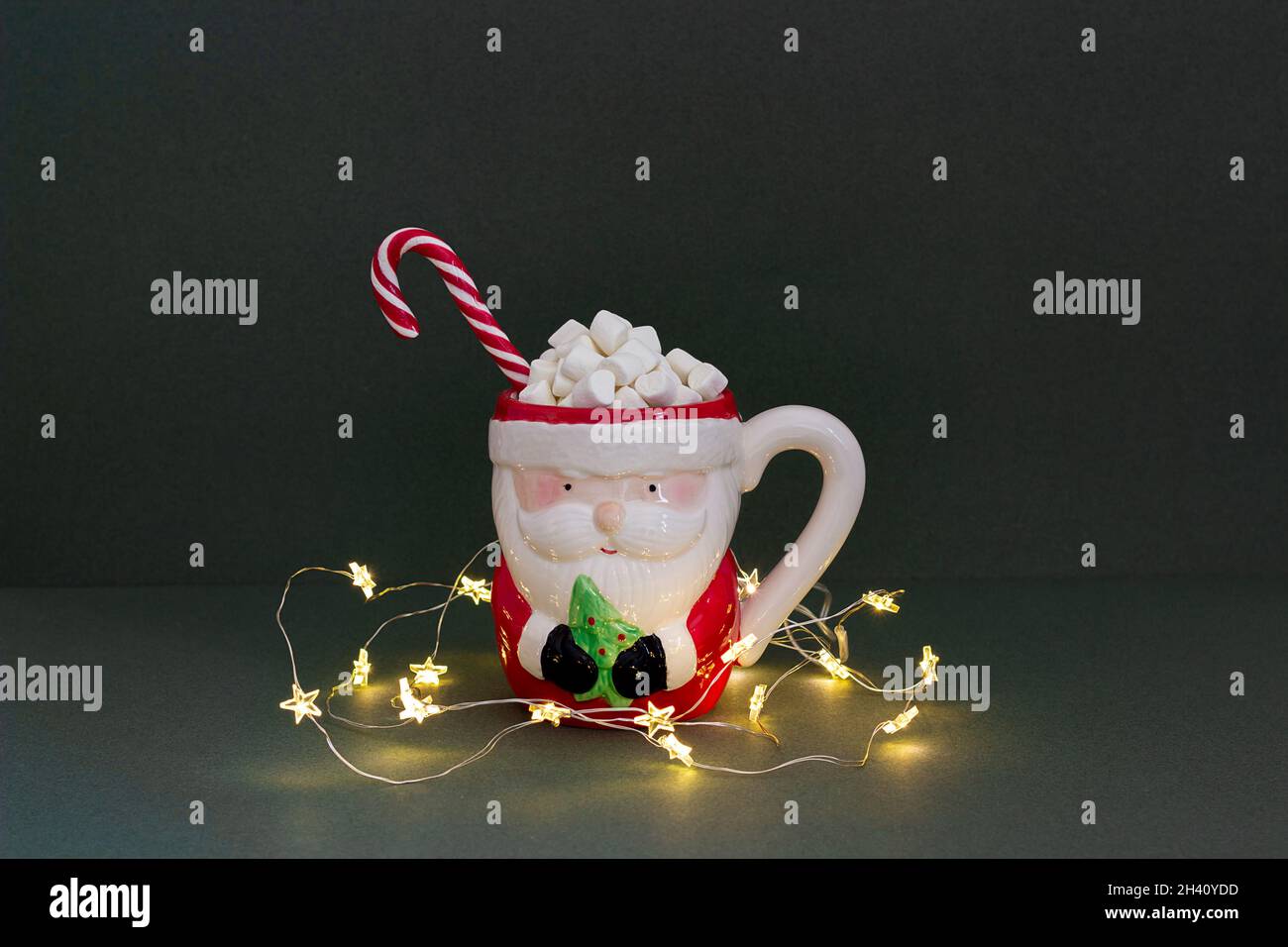 Buon Natale o Capodanno concetto. Divertente tazza di babbo natale di cacao con marshmallows, caramelle e luci di natale su sfondo verde. Mi Foto Stock