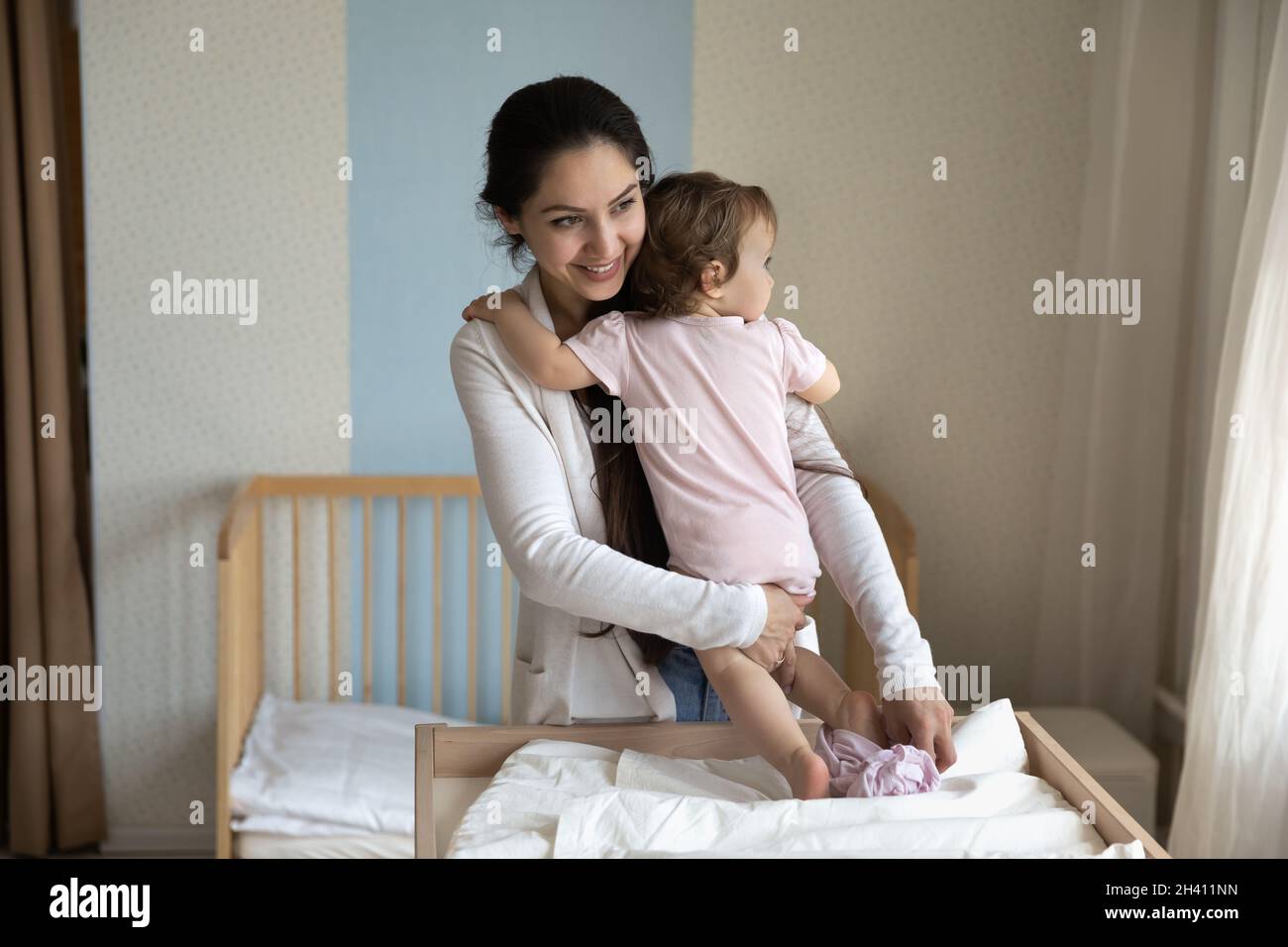 Sorridente giovane madre cura cambiare vestiti del bambino, pannolino sul tavolo Foto Stock