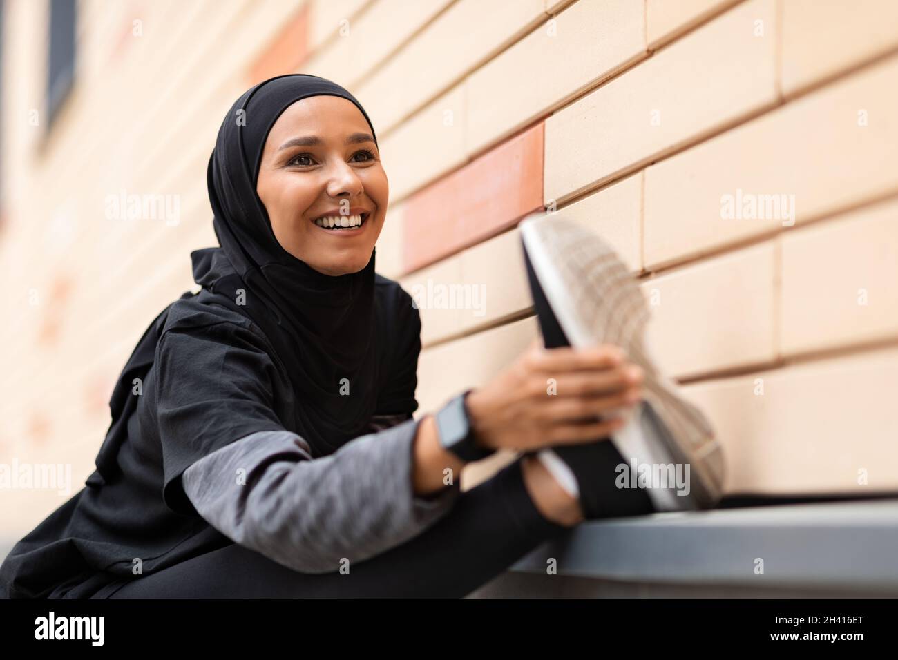 Atletica musulmana Lady in Sportswear riscaldamento prima di jogging all'aperto, allungando i muscoli delle gambe Foto Stock