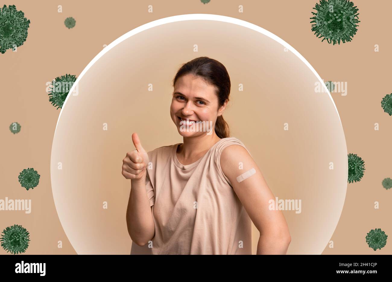 Sorridente giovane donna europea che mostra spalla con aiuto banda dopo l'iniezione e pollice in su segno nella bolla di protezione del virus Foto Stock