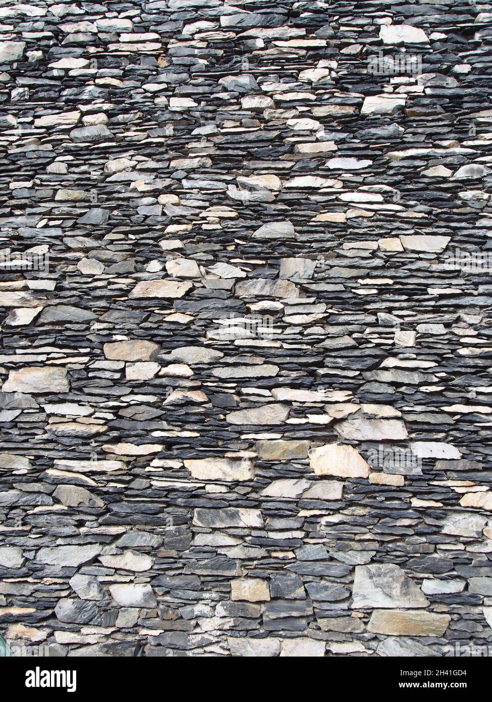 Vecchio muro di pietra grigio irregolare fatto di pezzi irregolari impilati di roccia Foto Stock